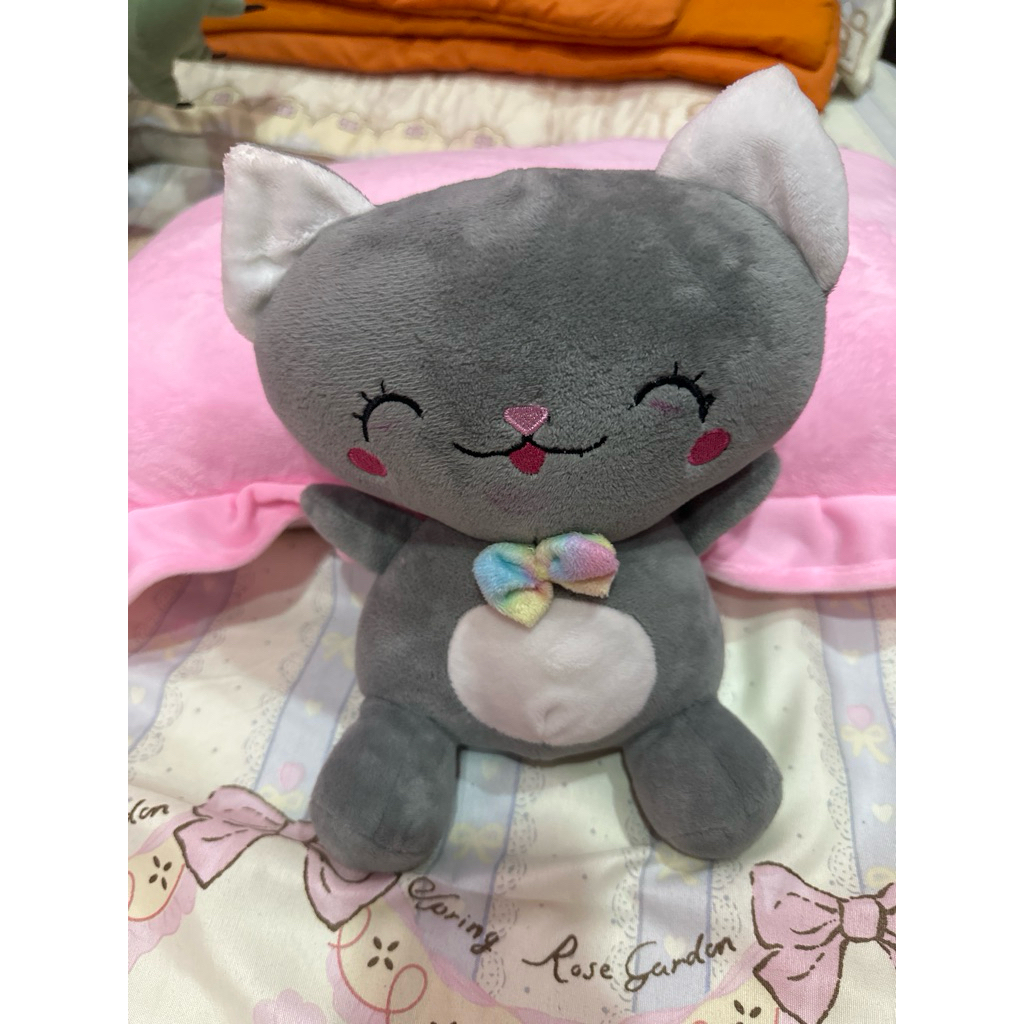 boneka kucing berwarna abu-abu dengan pita pelangi di lehernya
