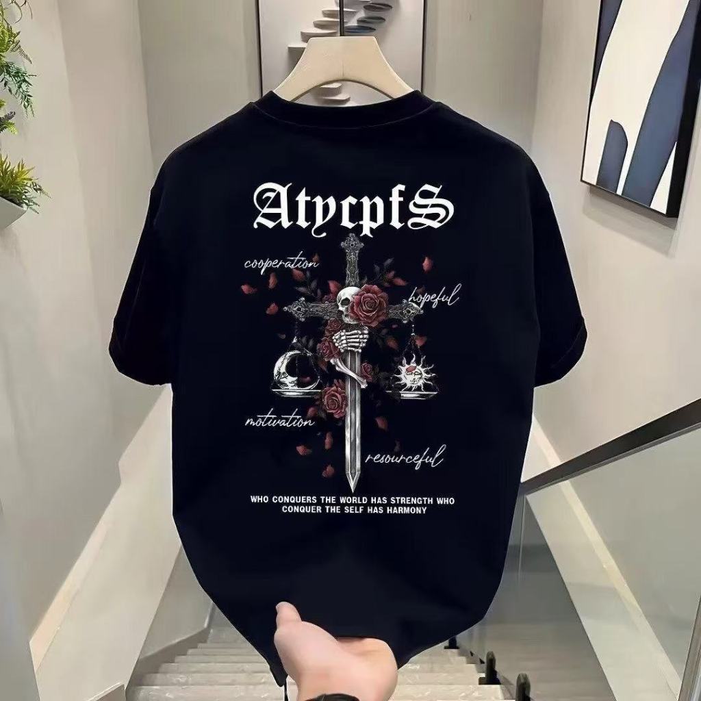 Kaos T-shirt dengan Desain Salib, Tengkorak, Bunga Mawar, dan Timbangan dengan Teks "AtypctS" serta 
