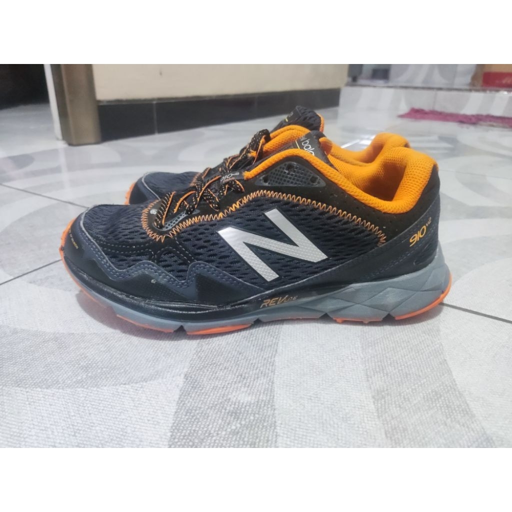 sepatu lari trail New Balance 910v2 pria berwarna hitam dan oranye dengan midsole REVlite.
